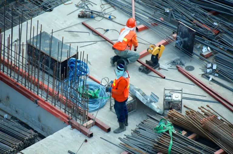 Construction workers arranging rebar and tools on a concrete floor in an outdoor site