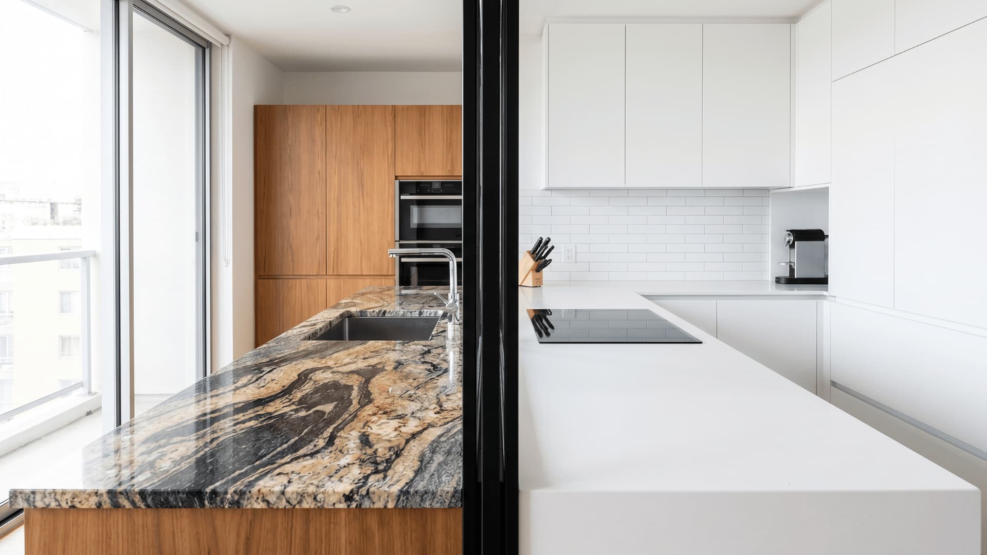 Modern kitchen split view with black vertical divider, granite countertop with natural patterns on left and white quartz countertop with smooth uniform finish on right
