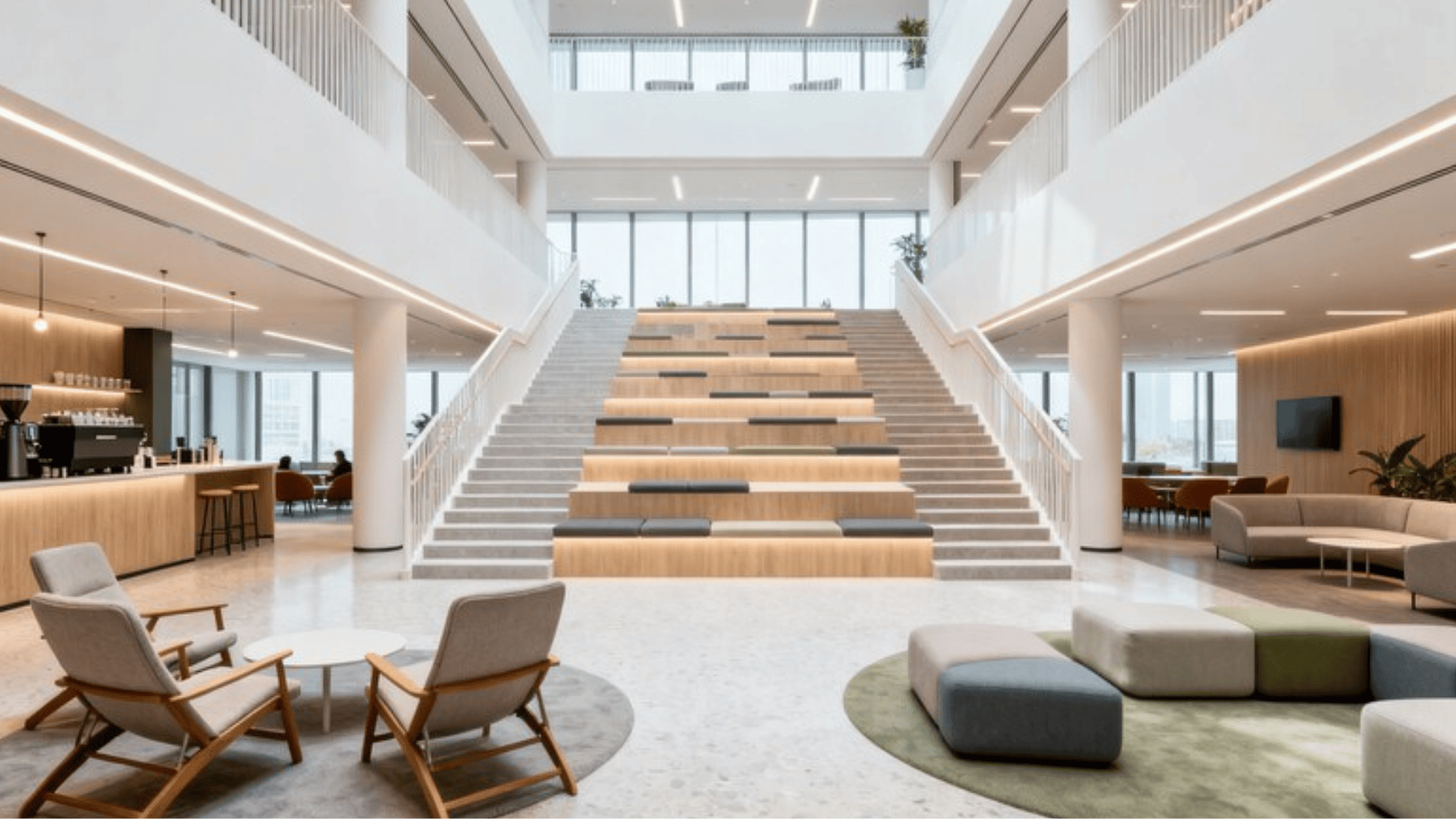 modern office atrium with tiered seating stairs, café area, lounge chairs, and open collaborative workspace