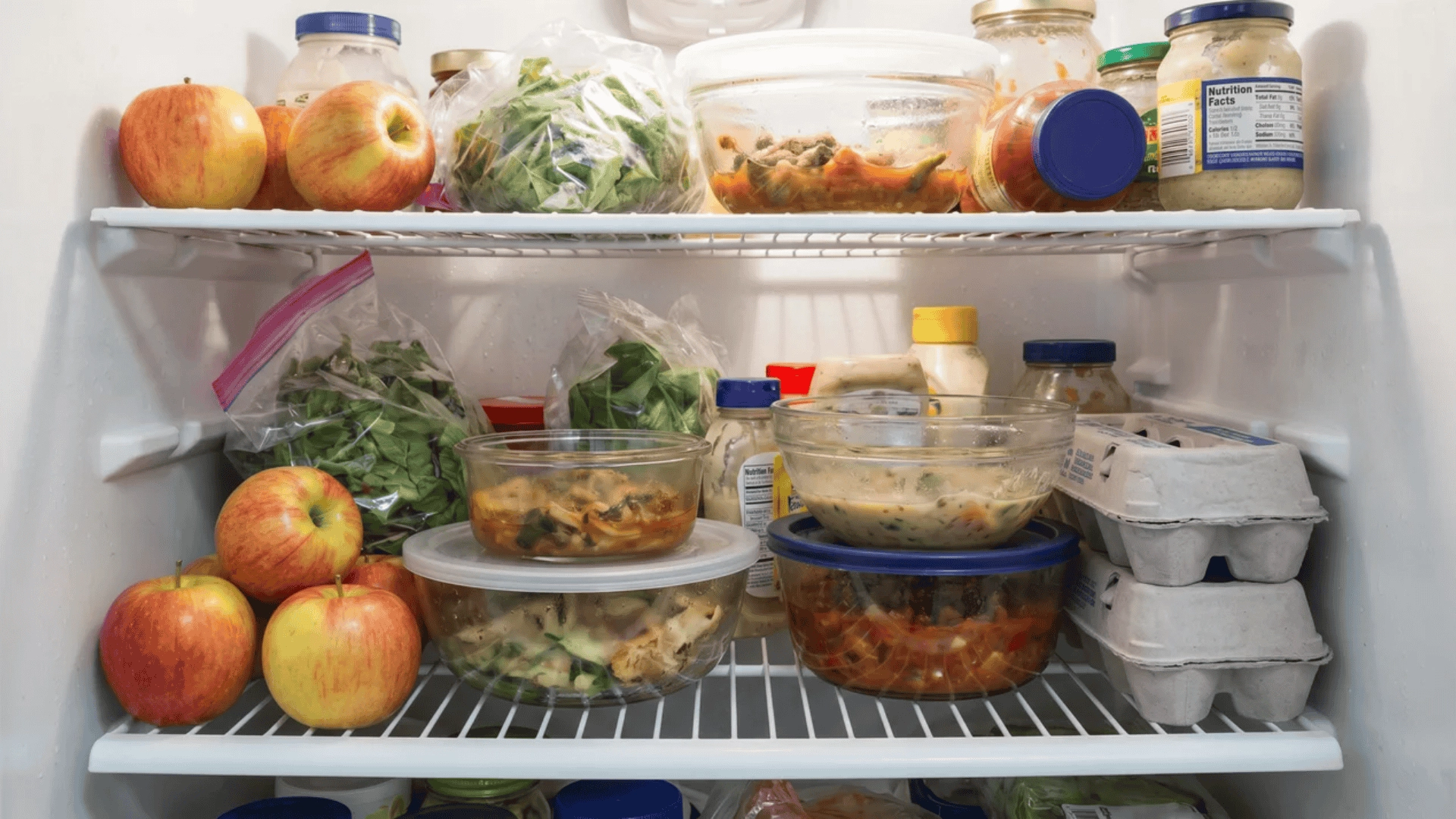 Overcrowded refrigerator shelf with mixed fruits, vegetables, and uncovered containers