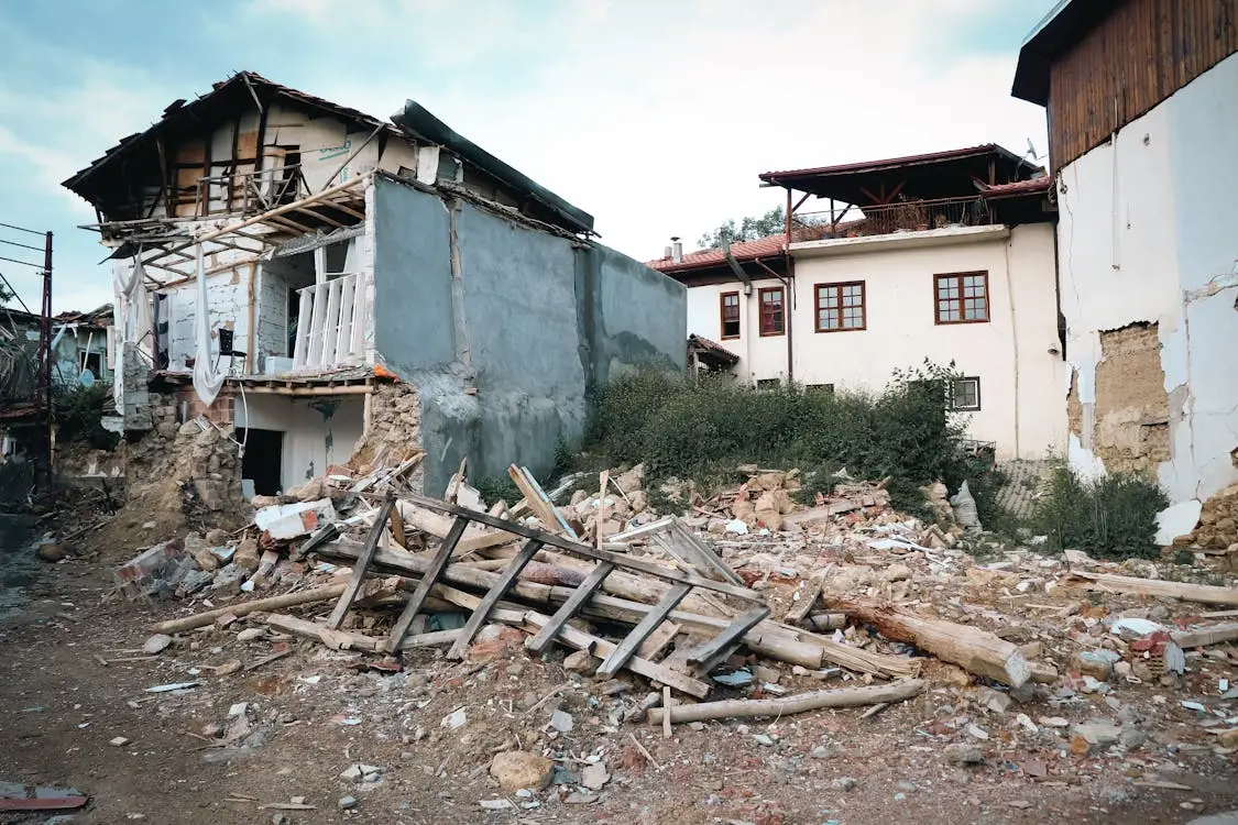 Partially collapsed building with debris and rubble in residential area under clear sky