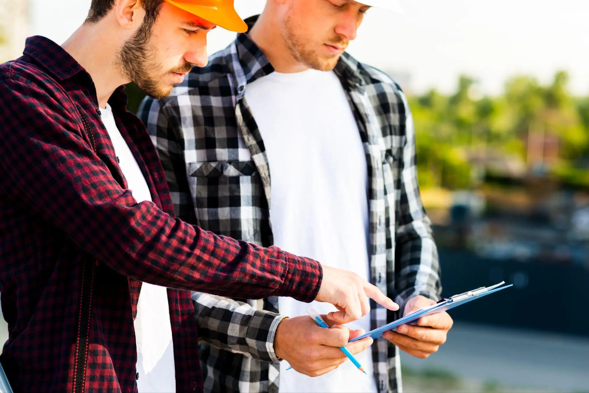 Two men in plaid shirts reviewing clipboard outdoors with tools in hand