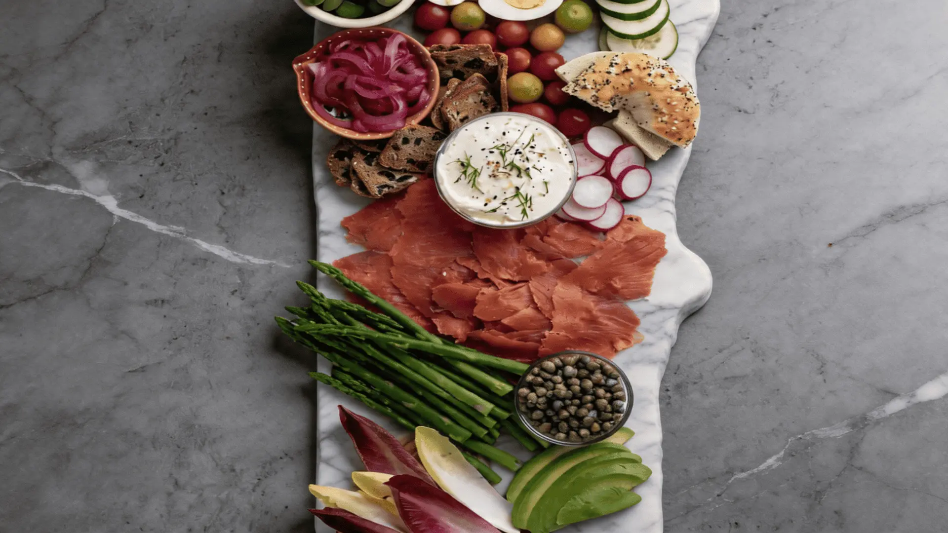 Salmon breakfast charcuterie board with smoked salmon, cream cheese, capers, red onion, and toasted bagels arranged on a marble surface.