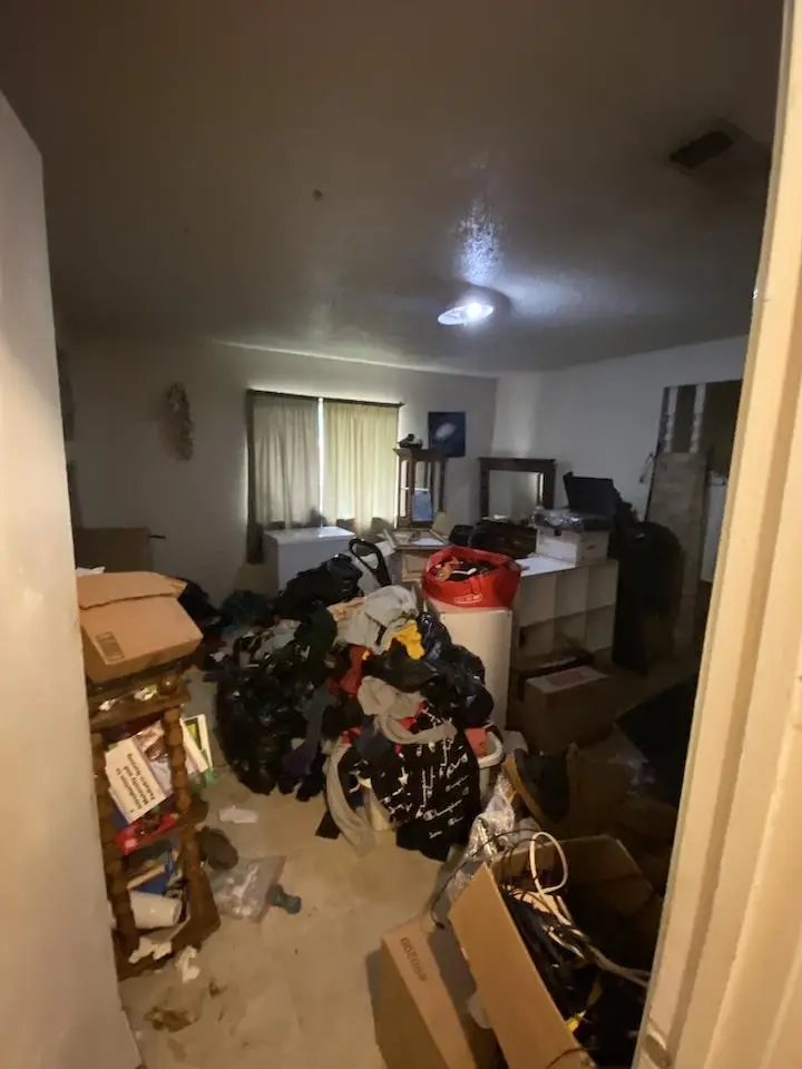 Dimly lit room with piles of clothes and cardboard boxes scattered on the floor