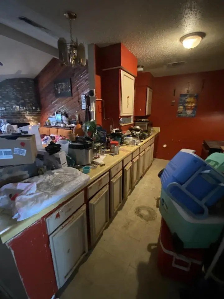 Cluttered kitchen with red walls, wooden cabinets, and various appliances under dim lighting