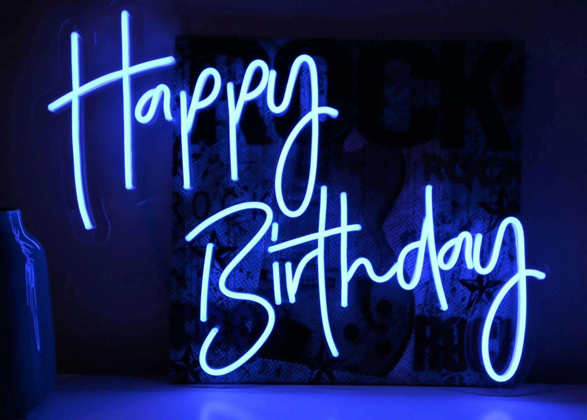 Neon blue "Happy Birthday" sign glowing in a dark room with decorative backdrop