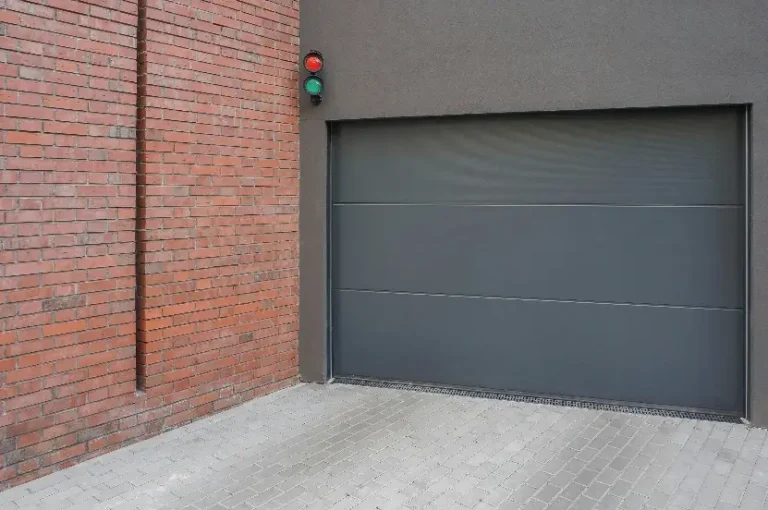 Gray garage door next to red brick wall with traffic light above on paved driveway