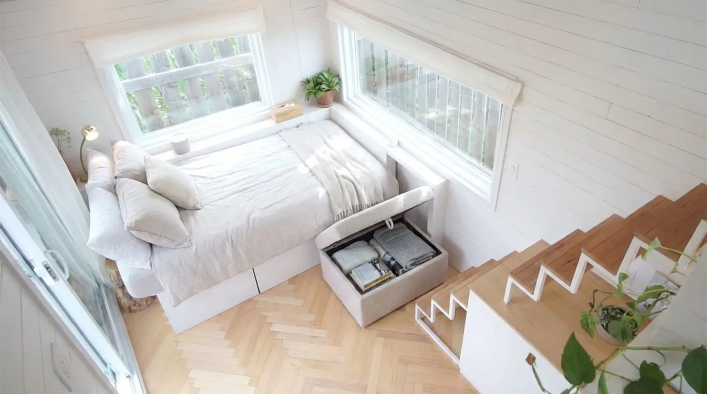 Tiny house living area with sofa bed, foldable table, and ottoman with hidden storage inside.