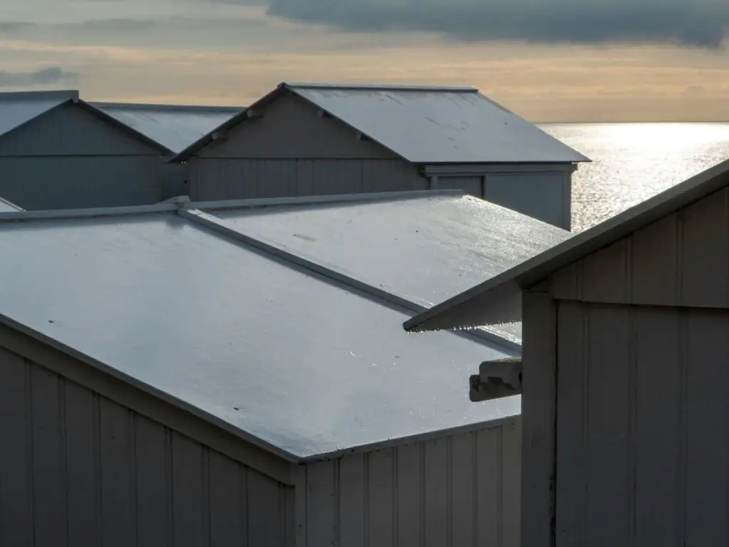 Rows of beach huts with shiny roofs overlooking a calm sea in overcast light