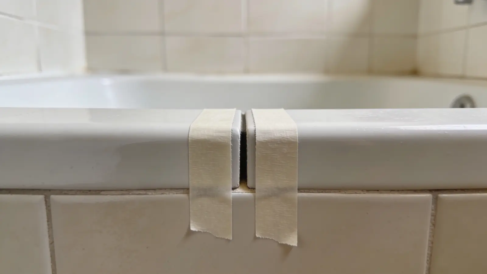 Two painter's tape strips placed above and below bathtub wall joint leaving narrow gap