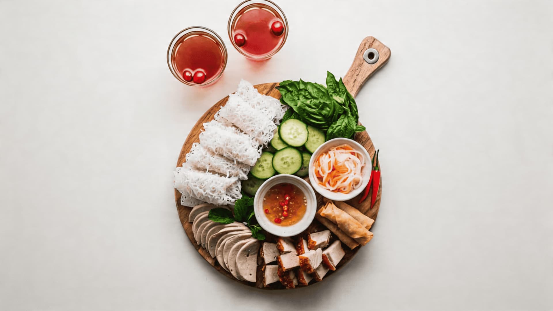 Vietnamese banh hoi charcuterie board with rice noodle sheets, fresh herbs, grilled protein, and dipping sauces in a unique and elegant spread.