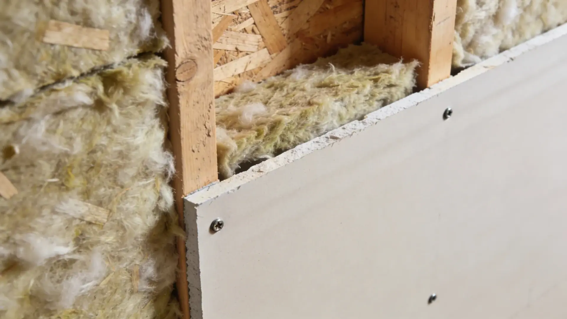 Wall frame filled with insulation material and partially covered with drywall panels