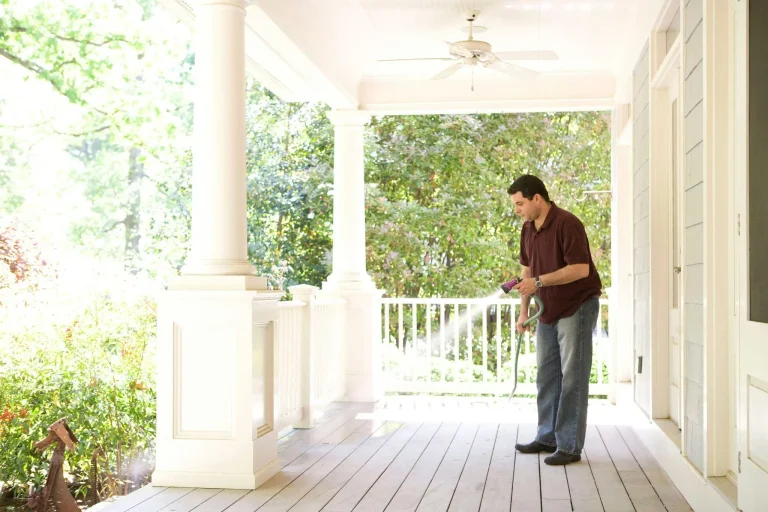 Man watering plants on a sunlit porch surrounded by lush greenery