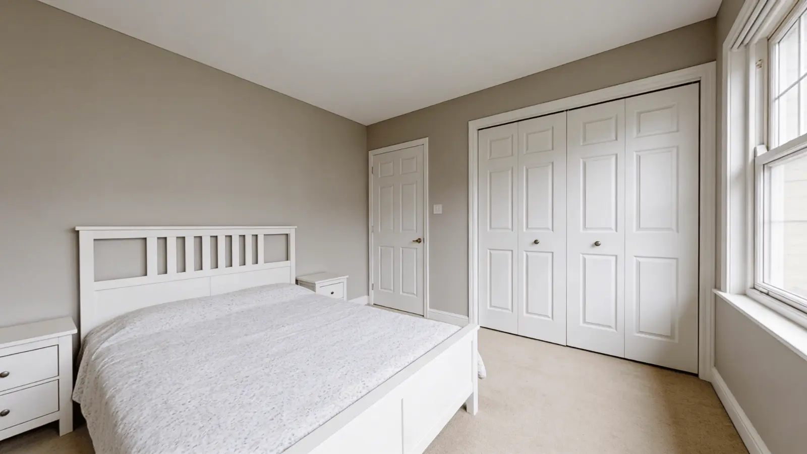 Wide bedroom view with Mega Greige walls, bed, door, wardrobe, and window in natural light