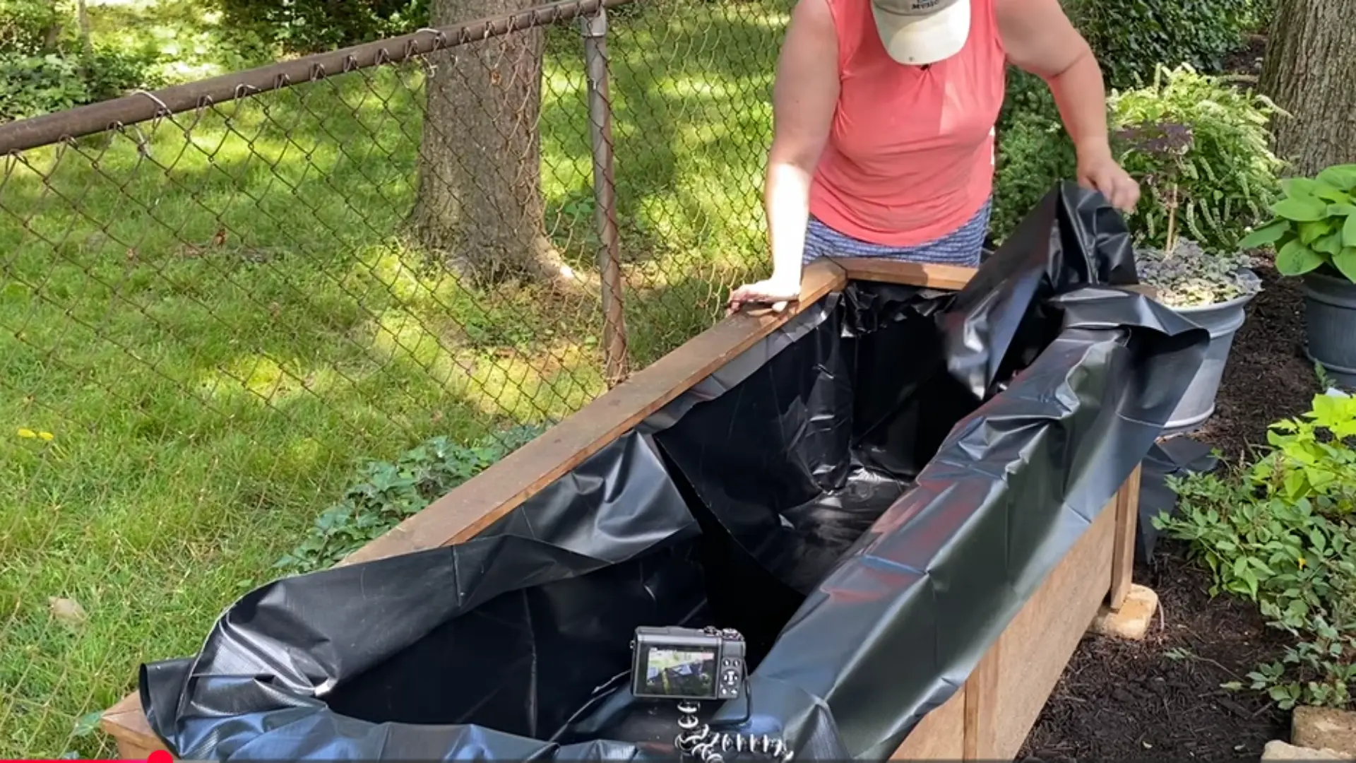 Person placing black pond liner inside a long wooden planter or raised garden bed outdoors
