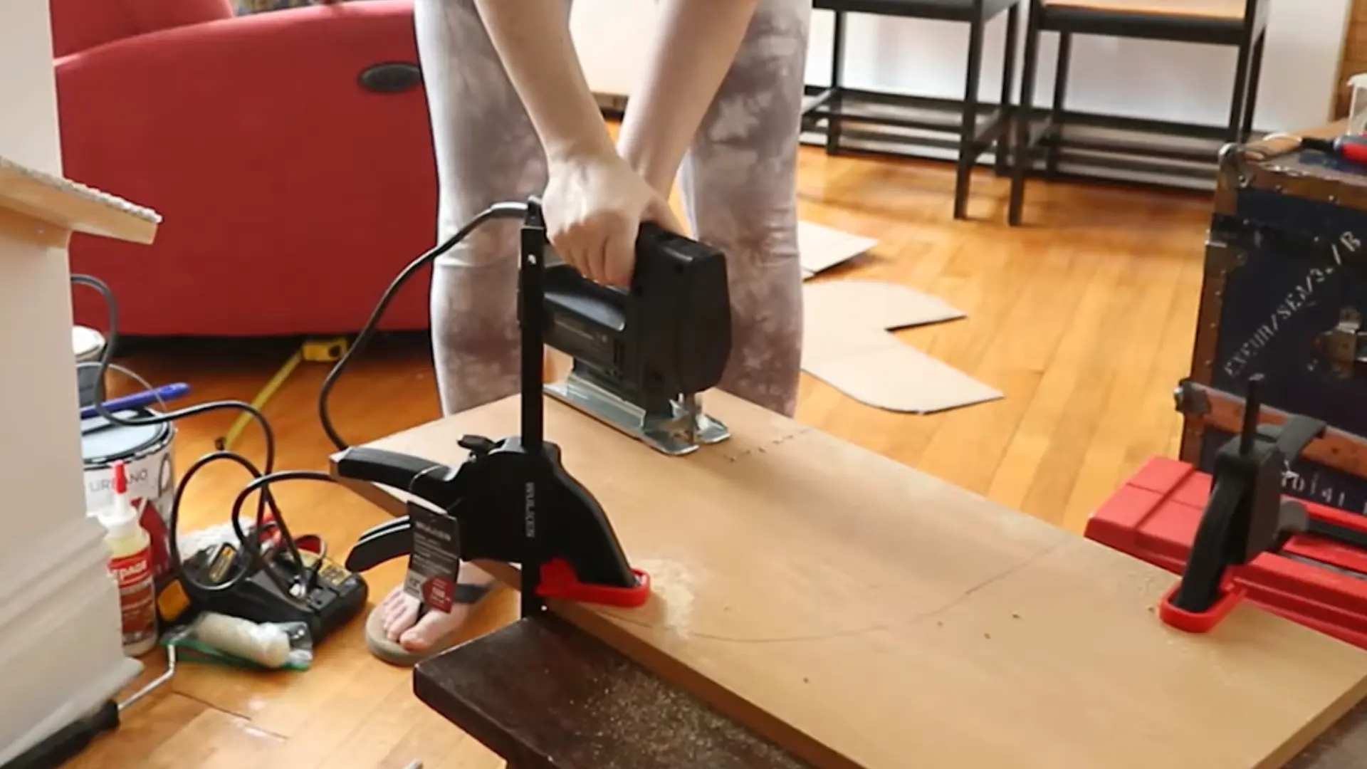 Person using a jigsaw to cut a wooden board clamped to a table indoors