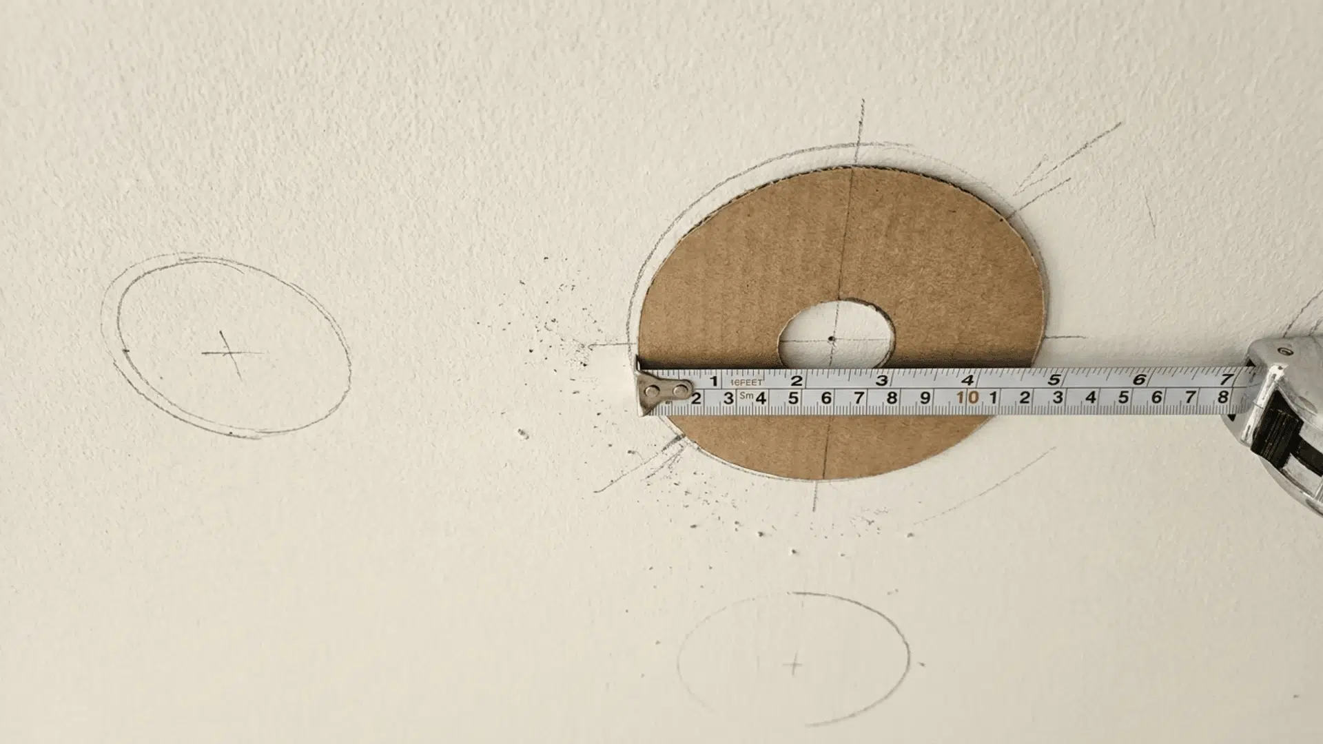 A ceiling with marked spots for recessed lights, using a tape measure and template for precise placement.