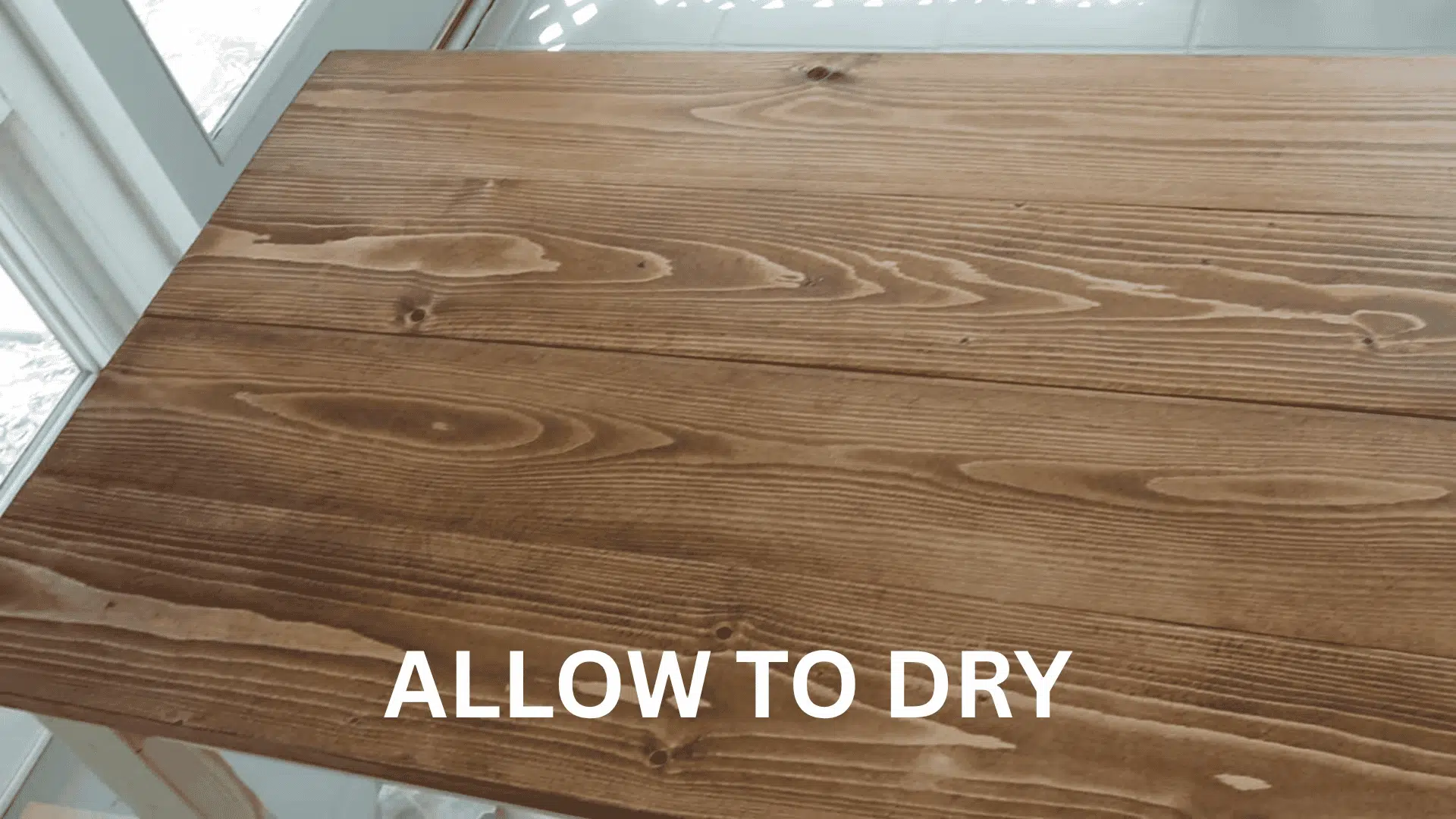 A close-up view of a wooden tabletop after the wood stain has been applied and dried, showing a rich brown grain.