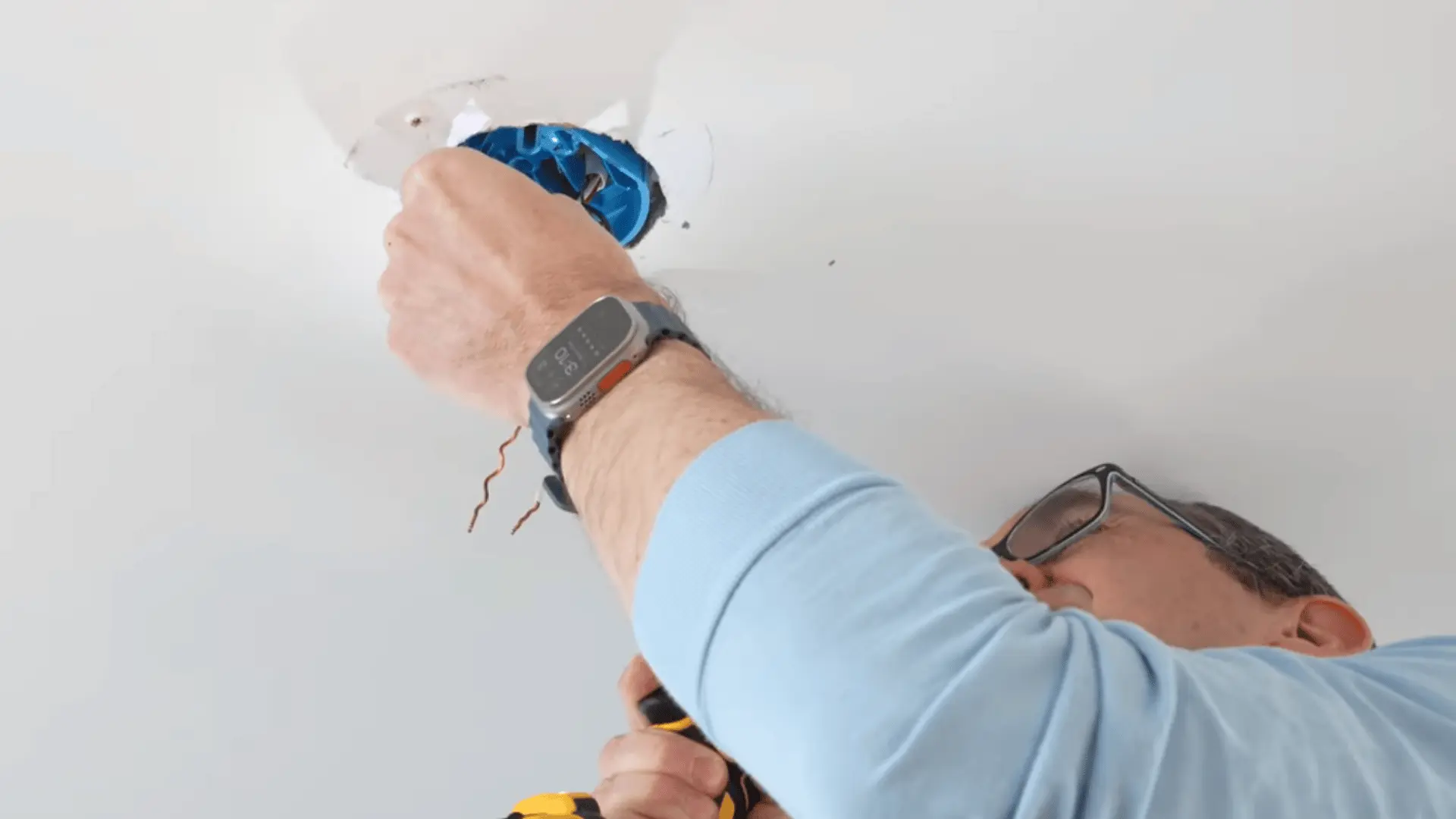 A person removing the old electrical box from the ceiling while preparing for new fan installation