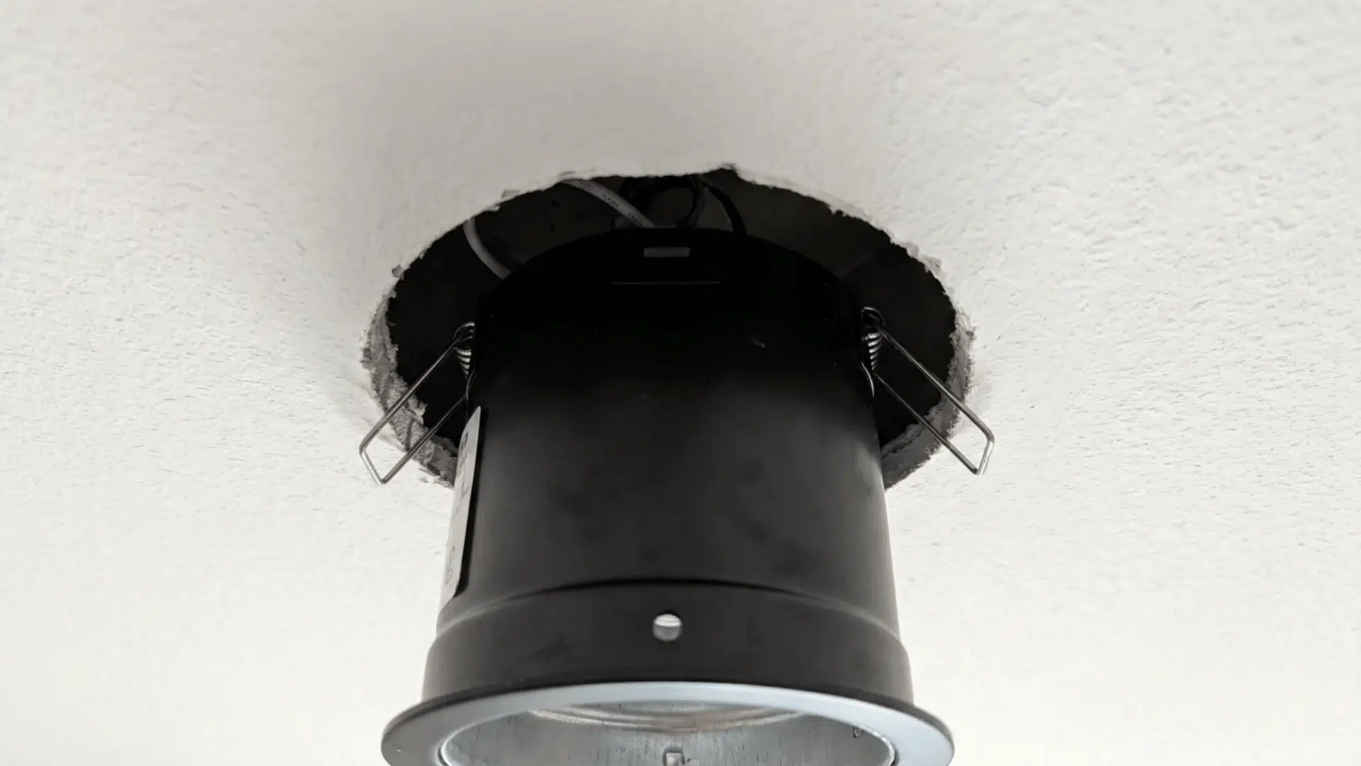 A recessed light can being placed into the ceiling hoSpring clips or brackets securing a recessed light can in place within the ceiling hole for stability.le, ensuring it fits snugly and flush.