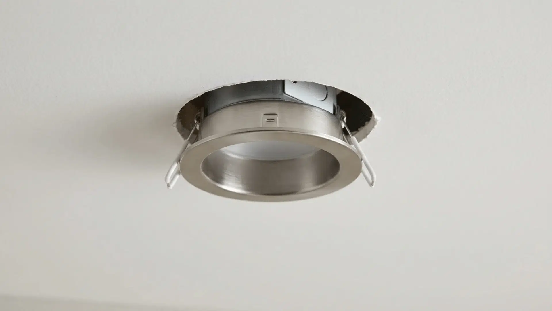 A recessed light can being placed into the ceiling hole, ensuring it fits snugly and flush.