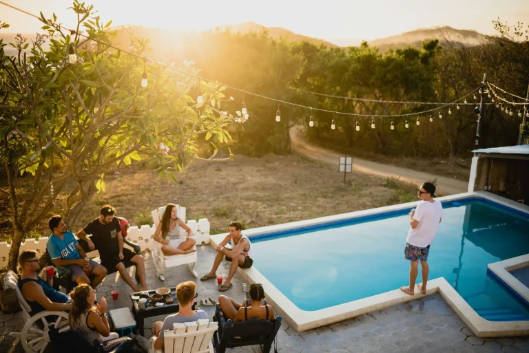 Group of friends relaxing by a swimming pool with drinks during sunset