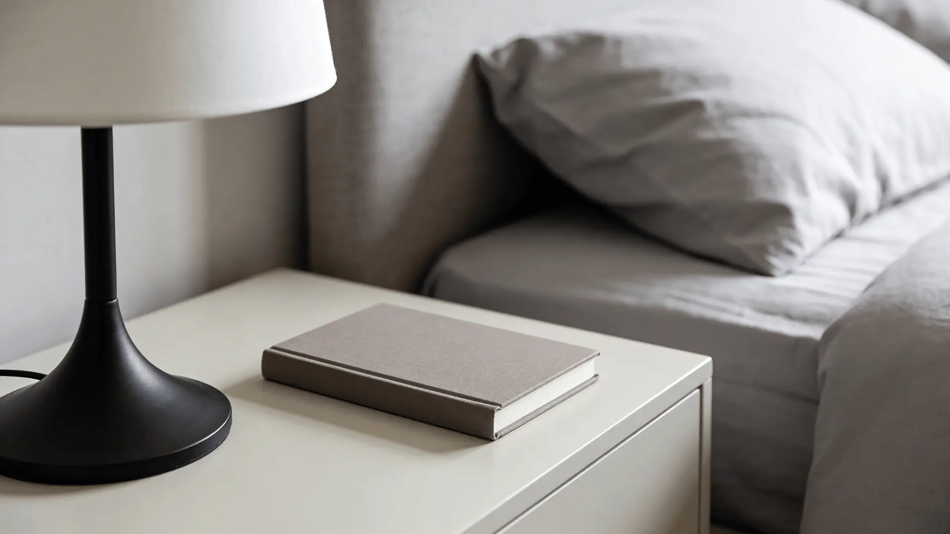 Bedside table next to a bed with a lamp and book within easy reach