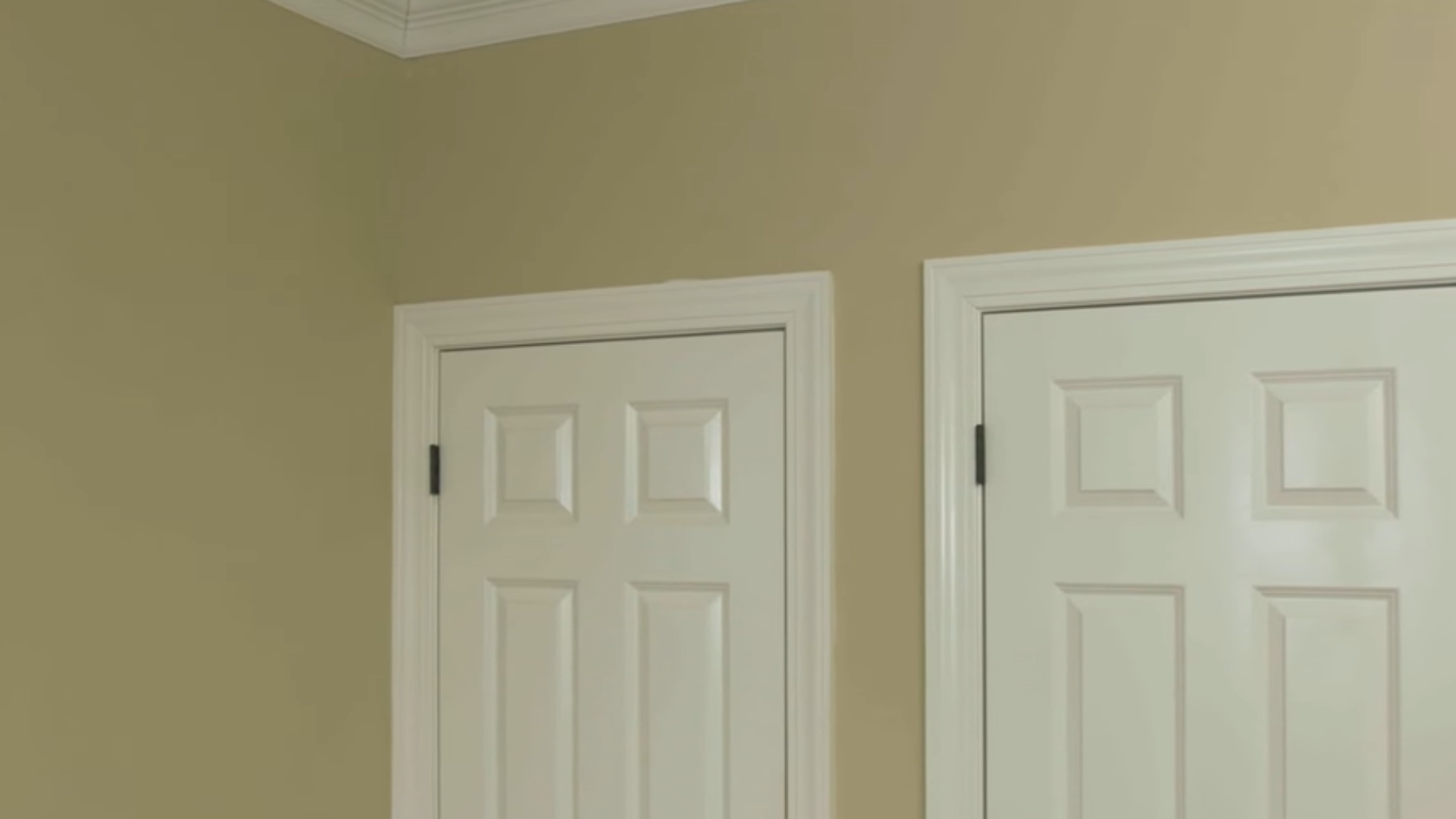 Beige wall with white trim and two white paneled being primed