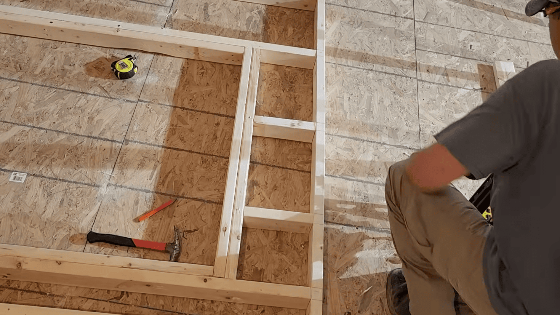 carpenter installing header and jack studs in a wall frame layout on the floor while preparing the framed opening for a door