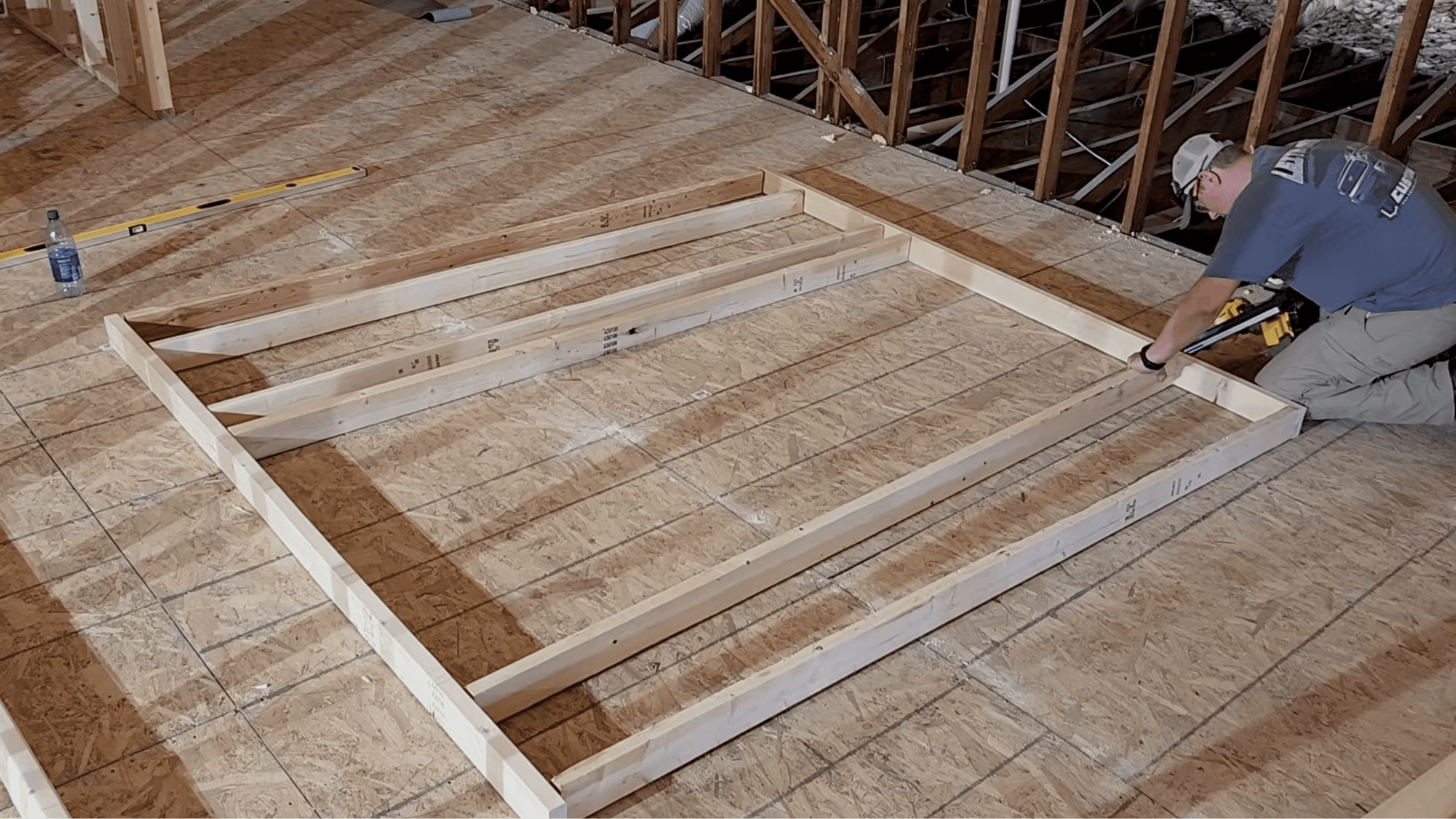 carpenter laying out wall framing lumber on the floor and fastening studs with a nail gun to assemble a wall frame before raising it