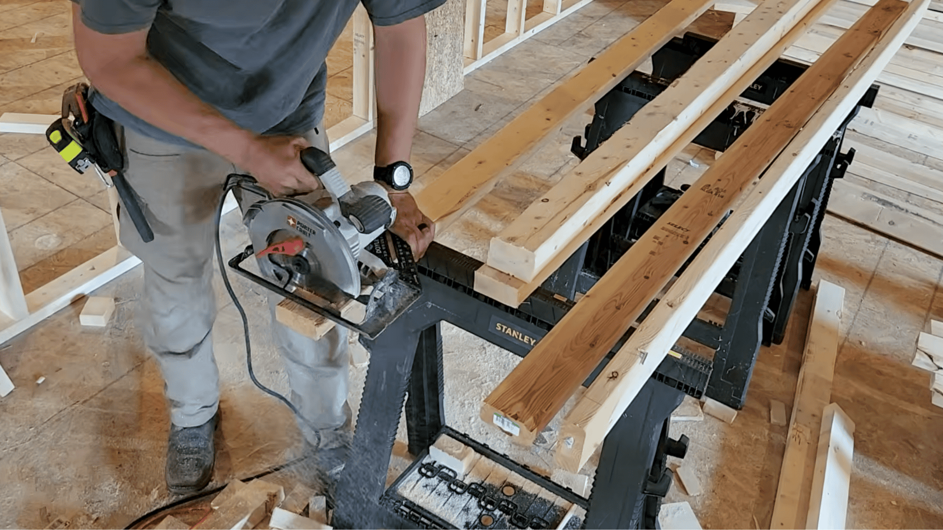 carpenter marking king and jack stud locations and cutting framing lumber with circular saw on sawhorses during wall framing
