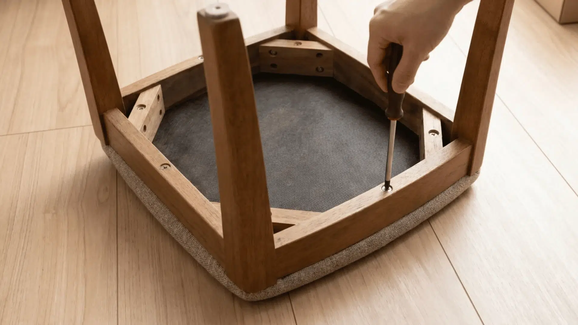 Chair turned upside down with screws being removed from seat base using screwdriver