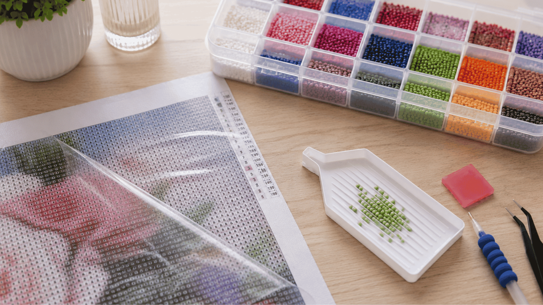 close up of a diamond painting canvas with a small section of protective plastic cover peeled back beside colorful resin diamonds and crafting tools on a clean table