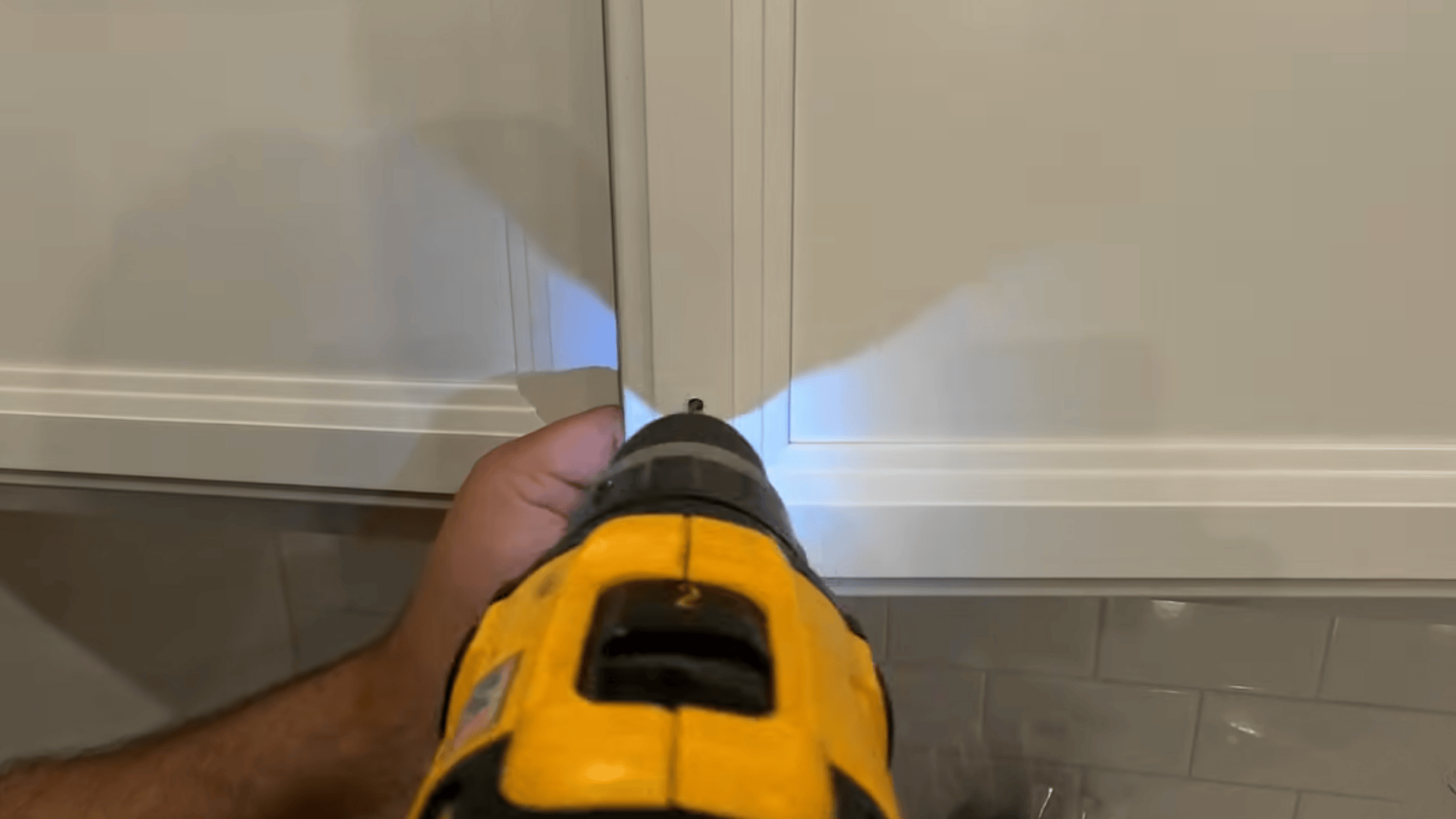 Close up of a drill creating a hole in a cabinet door at the marked spot for installing a handle