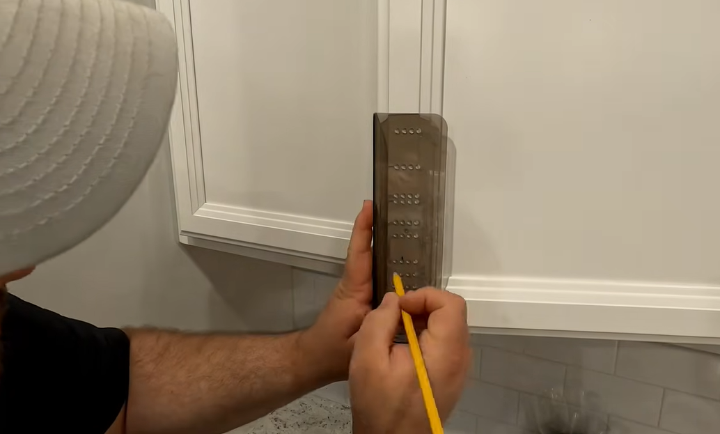 Close up of hands using a template and pencil to mark drill holes on a cabinet door for handle installation