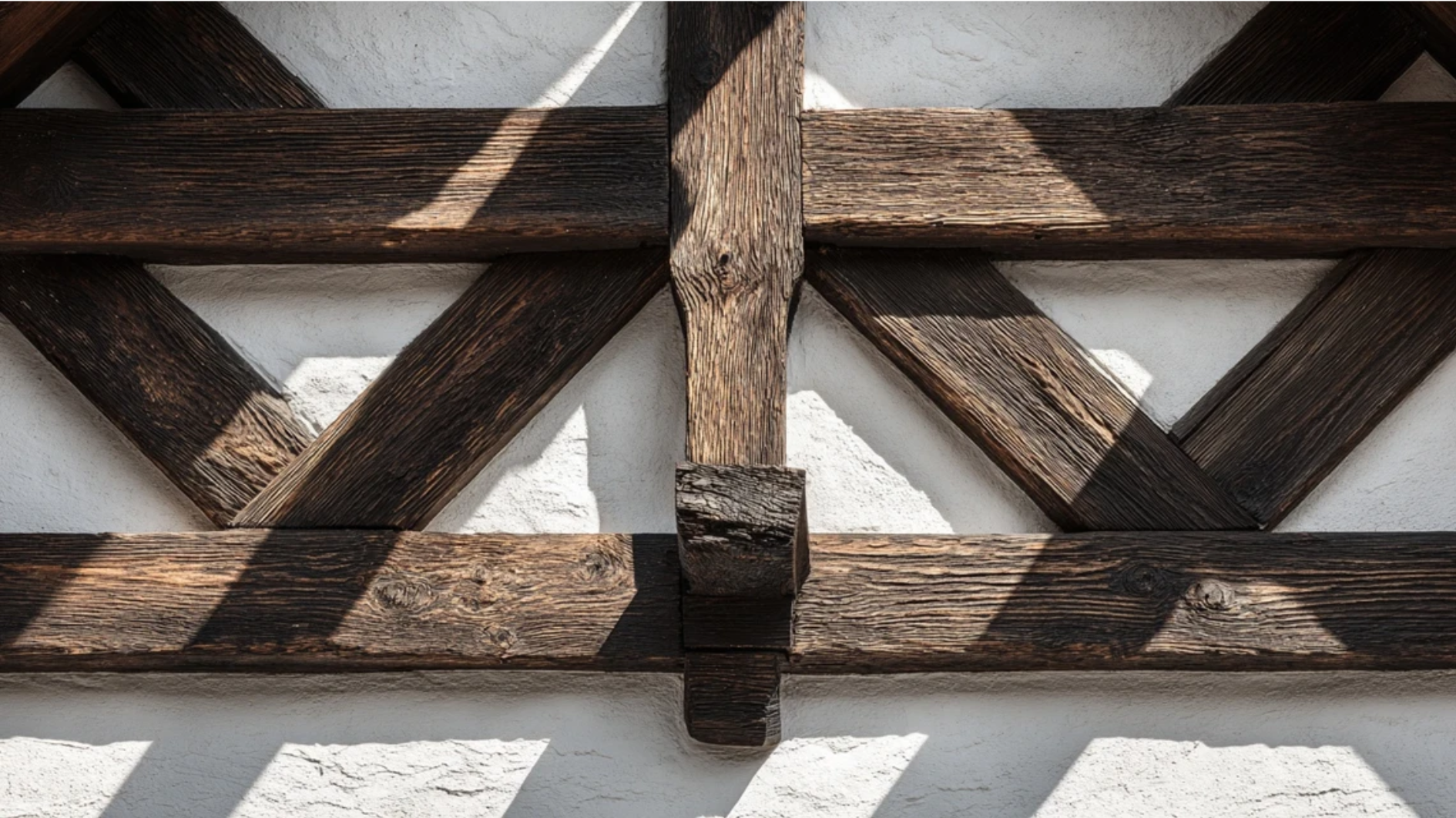 dark wooden beams in geometric patterns against white stucco wall showing classic Tudor Revival half-timbering detail