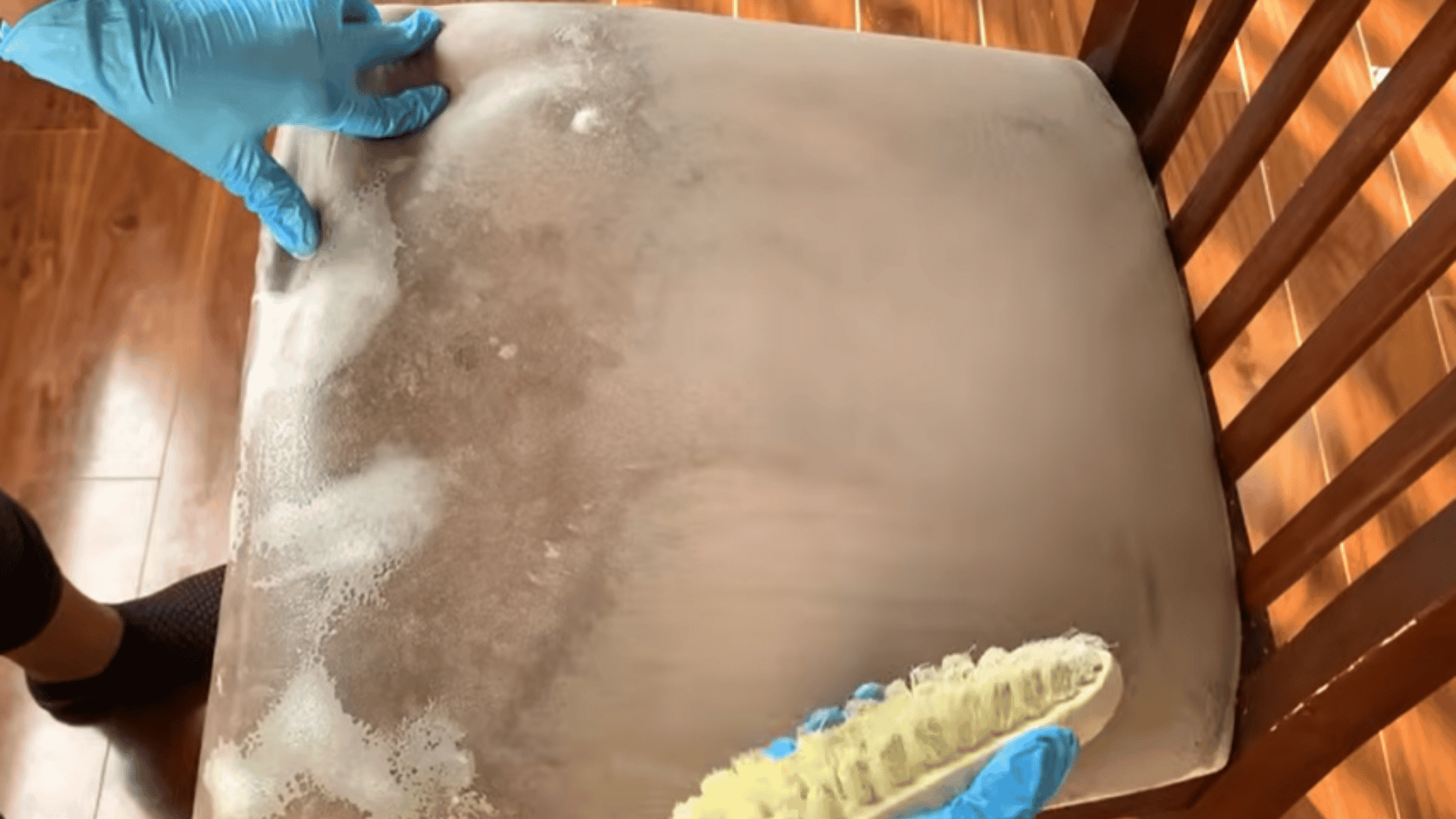 Gloved hands scrubbing a foam-covered upholstered chair seat with a brush