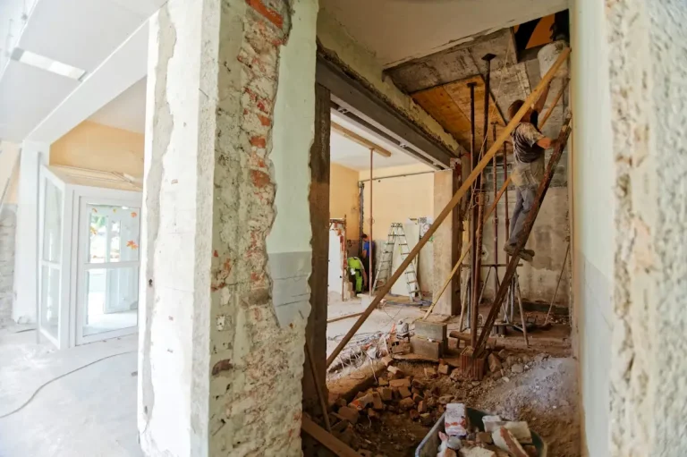 Construction worker on ladder in partially renovated building interior with exposed brick and debris