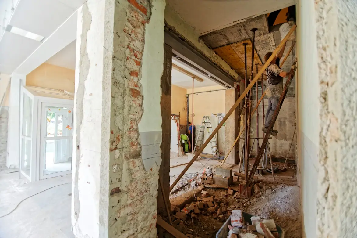Construction worker on ladder in partially renovated building interior with exposed brick and debris