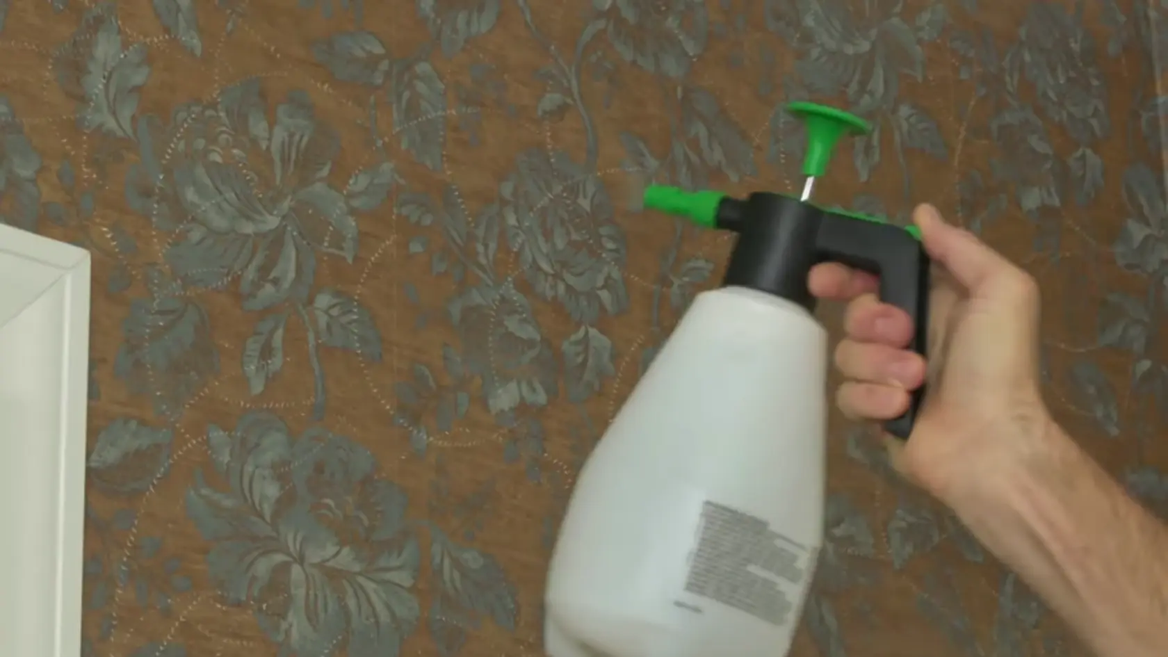 Hand spraying liquid onto floral wallpaper with a pump sprayer bottle