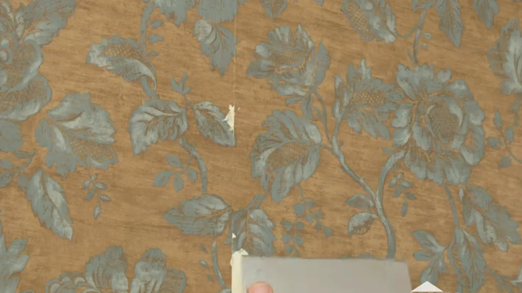 Hand using a scraper to remove patterned wallpaper from a wall