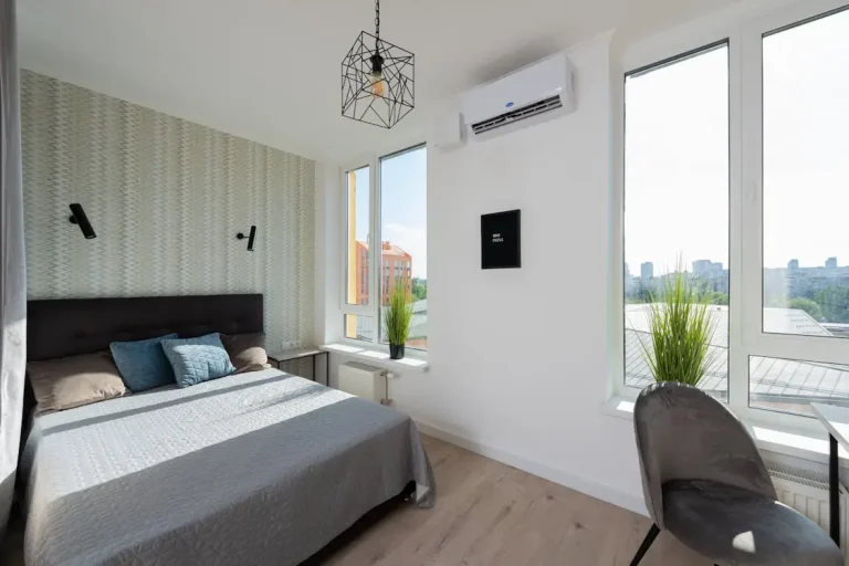 Modern bedroom with large windows, gray bedspread, and accent wallpaper under natural light