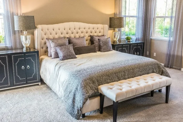 Luxurious bedroom with tufted headboard, patterned bedding, and beige bench in natural light