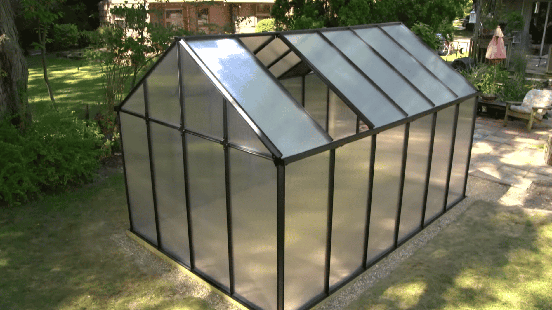 Installing clear greenhouse covering panels onto a backyard greenhouse frame during the construction process.