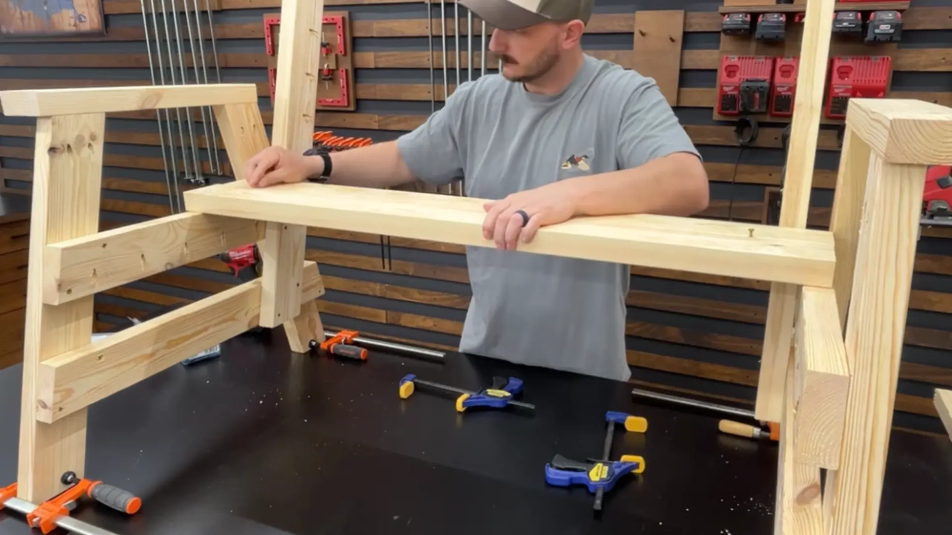 Man assembling a wooden frame on a workbench using clamps and screws in a workshop.