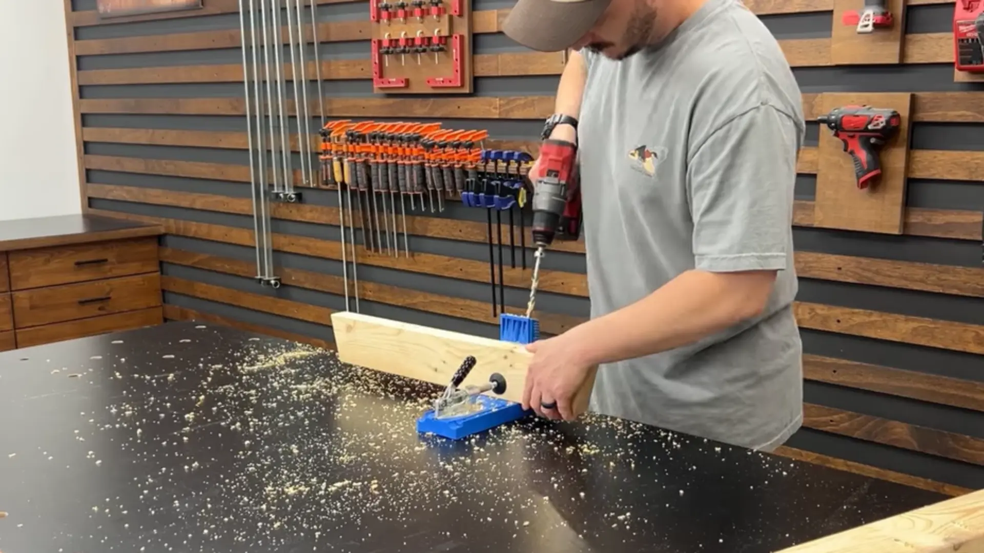 Man drilling a hole into a piece of wood clamped on a workbench in a workshop.