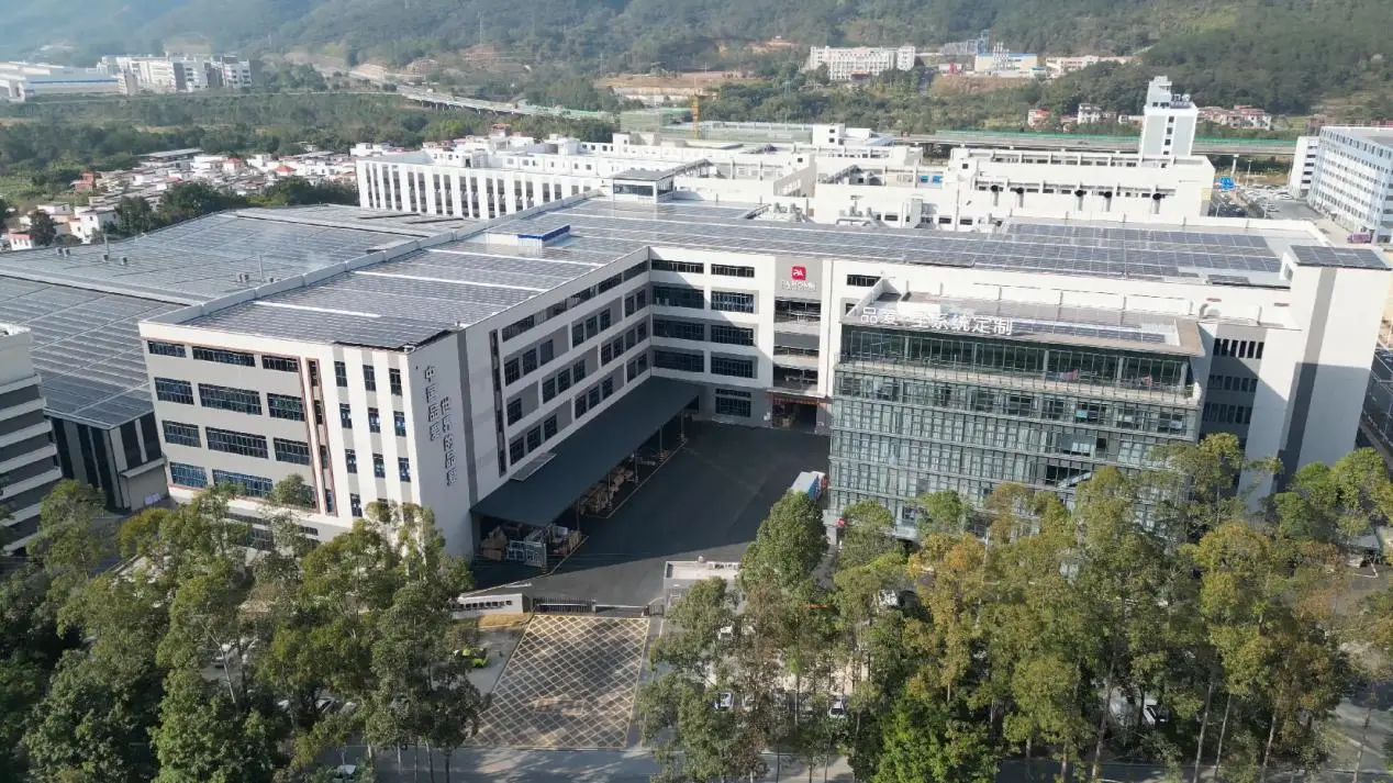 Large industrial building complex with solar panels surrounded by trees and hills in the background
