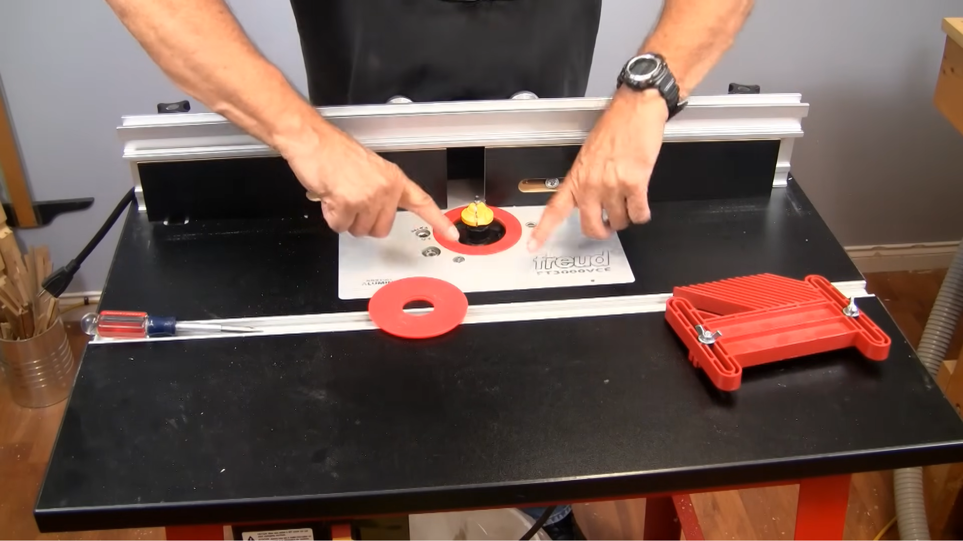person adjusting router bit on woodworking router table with safety tools