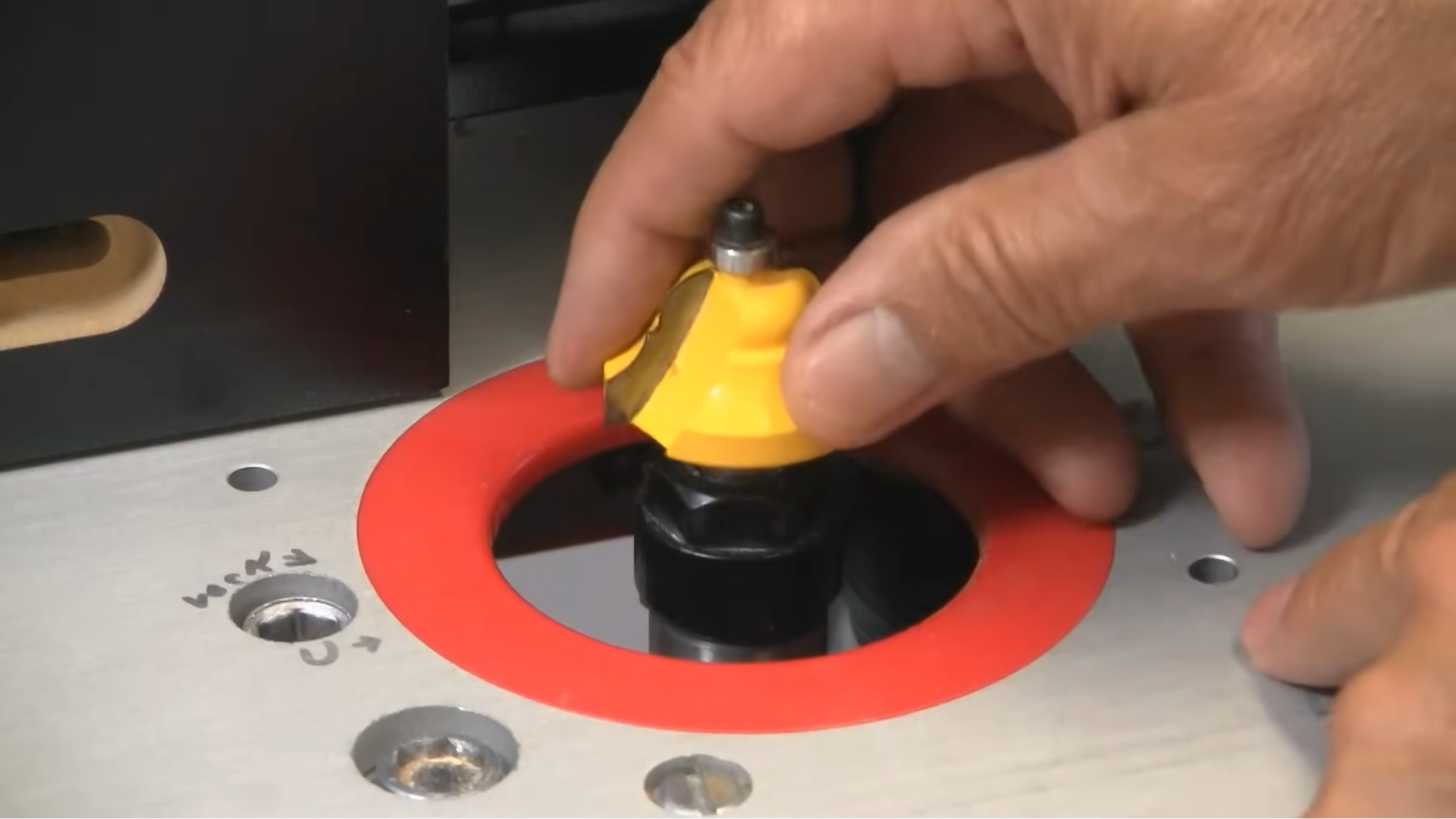 person adjusting router bit on woodworking router table with safety tools.