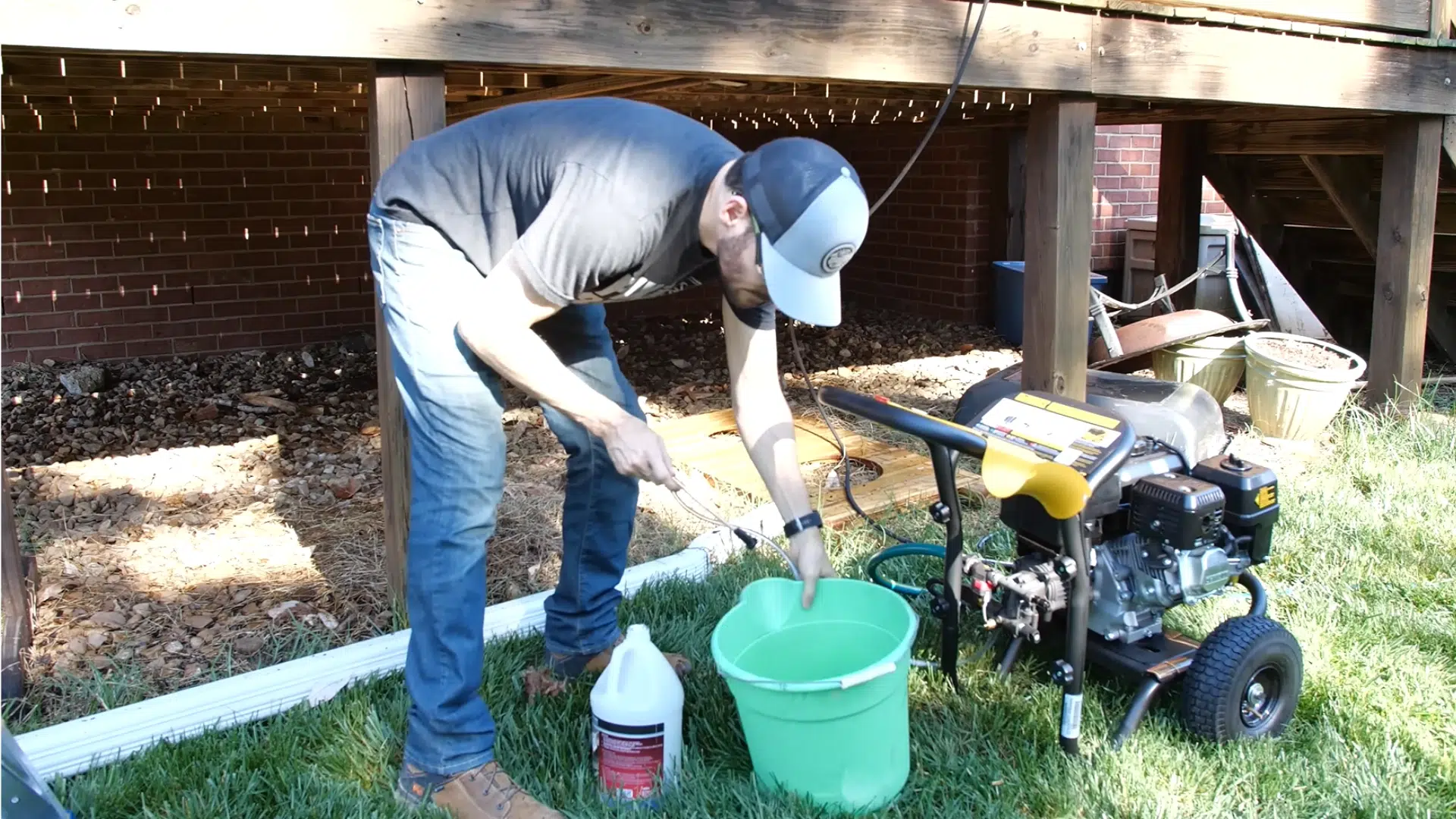 Person applying wood deck cleaner with oxalic acid through a siphon tube, preparing to rinse off residue with a pressure washer.